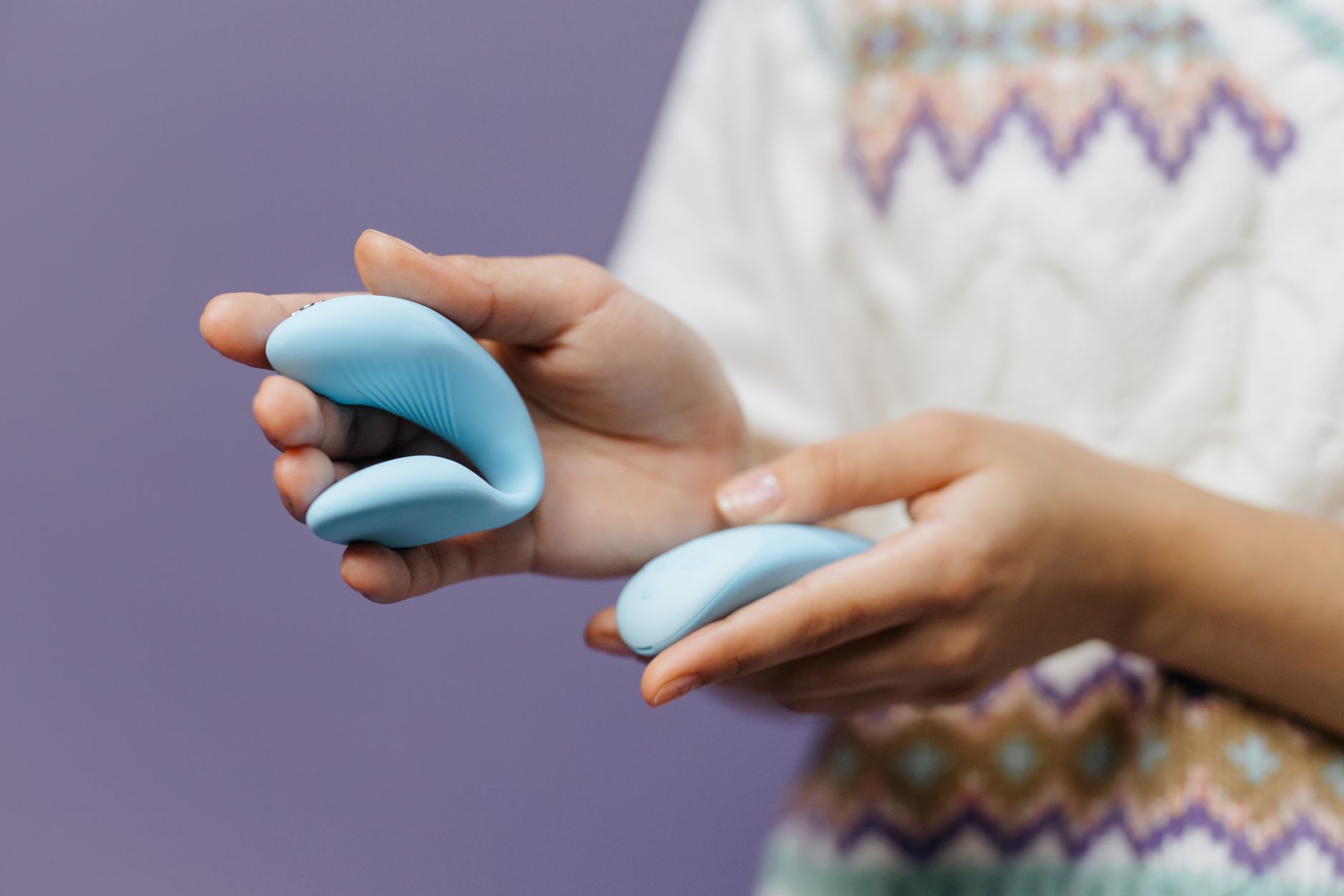 Close-up de mãos segurando um vibrador azul elegante contra fundo roxo, simbolizando intimidade e sensualidade moderna