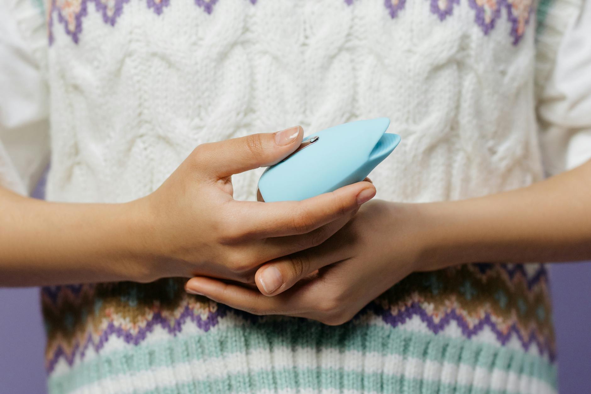 Mãos segurando vibradores de silicone azul e rosa em postura contemplativa